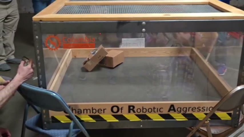 Two small combat robots pushing against each other inside a clear-walled arena labelled Chamber of Robotic Aggression